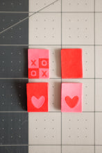 Load image into Gallery viewer, A vibrant flat lay of The Weekend Quilter's Hugs and Kisses woven labels in shades of pink, red, and pastel. The design includes "XOXO" motifs and reversible heart labels with light and dark sides, perfect for enhancing quilts, bags, and handmade sewing projects with a colorful, personalized touch.