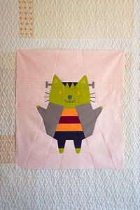 Patchwork quilt square with a colorful cat design on a textured background. The Weekend Quilter Halloween Catwalk Series Frankie Cat Mini Quilt Pattern
