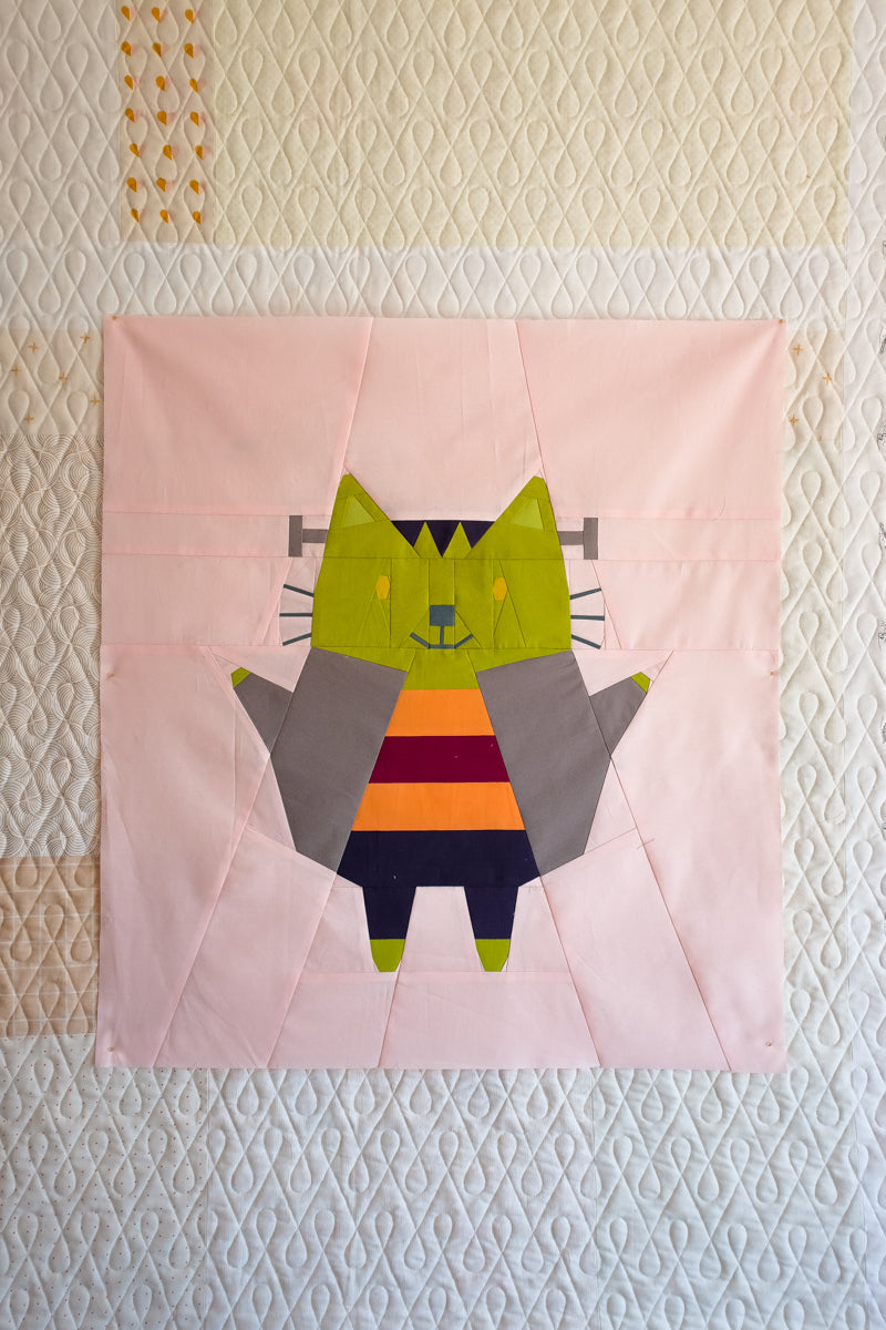 Patchwork quilt square with a colorful cat design on a textured background. The Weekend Quilter Halloween Catwalk Series Frankie Cat Mini Quilt Pattern