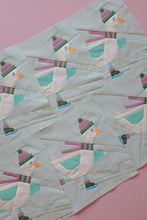 Load image into Gallery viewer, A close-up of a Frosty Flappers quilt blocks from the Beaks on Ice Series by The Weekend Quilter featuring a repeating pattern of stylized penguins in pastel colors on a pale mint green background, laid flat on a solid pink surface.
