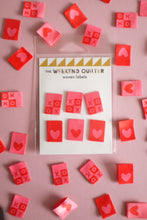 Load image into Gallery viewer, A vibrant flat lay of The Weekend Quilter&#39;s Hugs and Kisses woven labels in shades of pink, red, and pastel. The design includes &quot;XOXO&quot; motifs and reversible heart labels with light and dark sides, perfect for enhancing quilts, bags, and handmade sewing projects with a colorful, personalized touch.