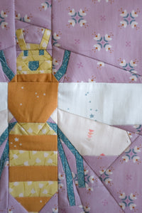 Quilt block with a yellow dress on a purple floral background. Pollen Gatherer foundation paper pieced (FPP) quilt block designed by The Weekend Quilter.  fabrics all from the GeoBloom Fabric collection for AGF 