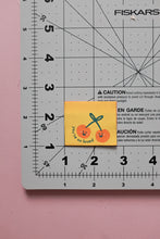 Load image into Gallery viewer, Small yellow card with cherries on a Fiskars cutting mat.